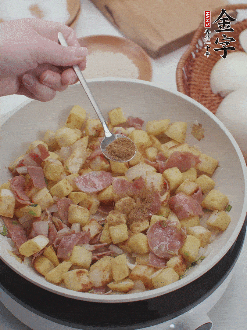 起鍋少油，煸香洋蔥丁、蔥白，加入金字培根火腿翻炒幾下，再加入饅頭丁、1小勺孜然粉、少許鹽翻炒均勻并鋪平。